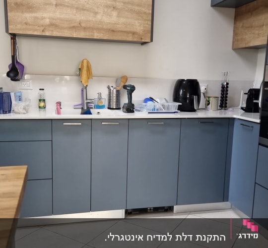 מטבח עם ארונות כחולים, כלים ומכשירים על השיש